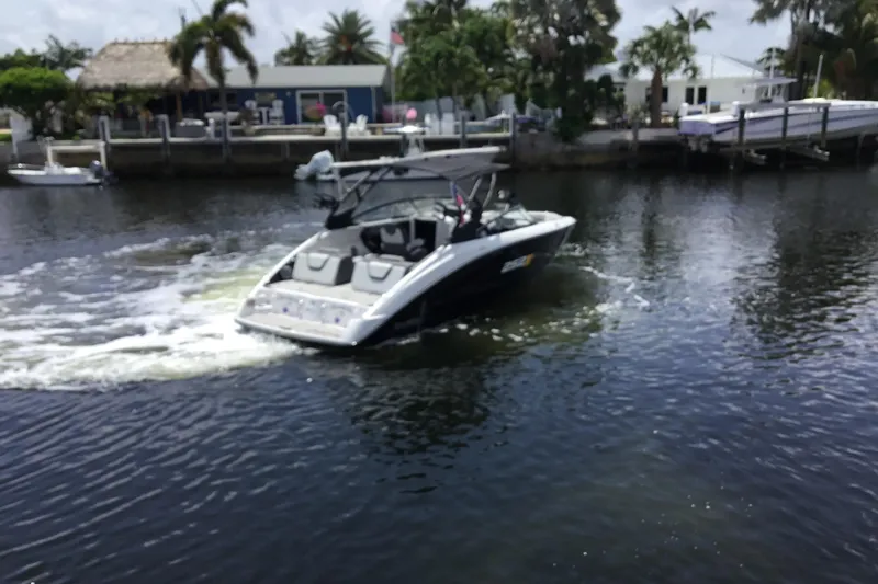 Slide: The Image of 2023 Yamaha Boats 252XE cruising on a calm waterway near a tropical dock. - 9