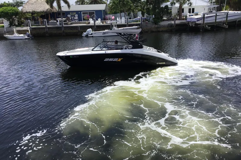 Slide: The Image of 2023 Yamaha Boats 252XE cruising on a calm waterway near a dockside residence. - 5
