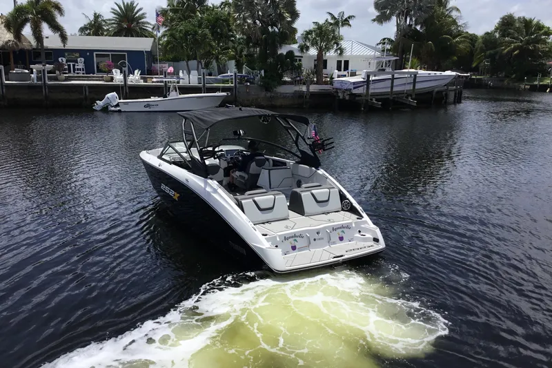 Slide: The Image of 2023 Yamaha Boats 252XE cruising on a scenic waterway near a dockside home. - 3