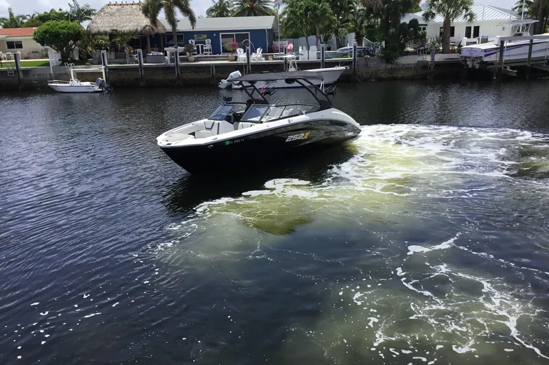 Slide: The Image of 2023 Yamaha Boats 252XE cruising on a calm waterway near a residential area. - 6