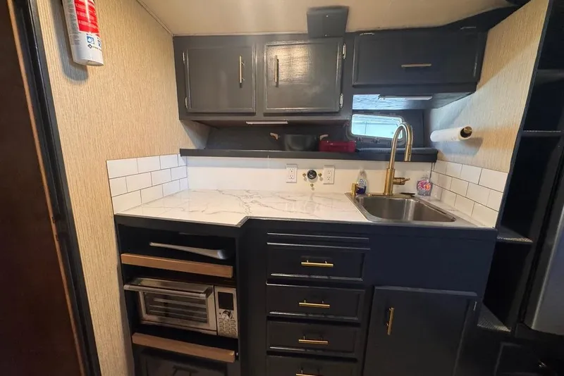 Slide: The Image of Compact kitchen in a 1982 Sunliner Ocean Yachts, featuring dark cabinets and marble countertop. - 33