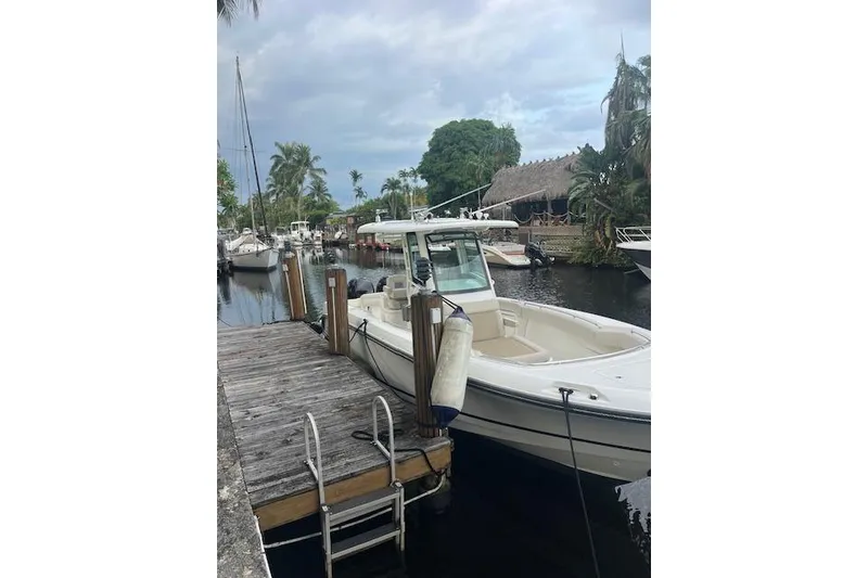 The Image of 2016 Boston Whaler 270 Dauntless docked by a wooden pier, surrounded by lush greenery. - 1