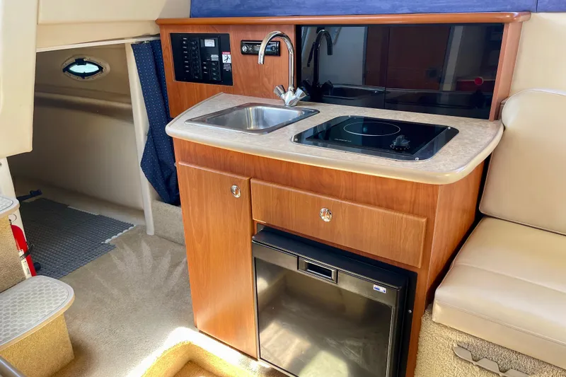Slide: The Image of 2008 Bayliner 265 boat interior with kitchenette, featuring sink, stove, and mini-fridge. - 16