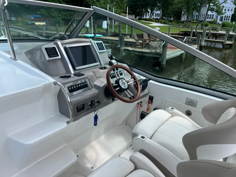 Slide: The Image of The image shows the cockpit of a 2013 Chaparral 330 Signature. It features a sleek design with a wooden steering wheel and modern instruments. A calm river and dock are visible in the background. - 15