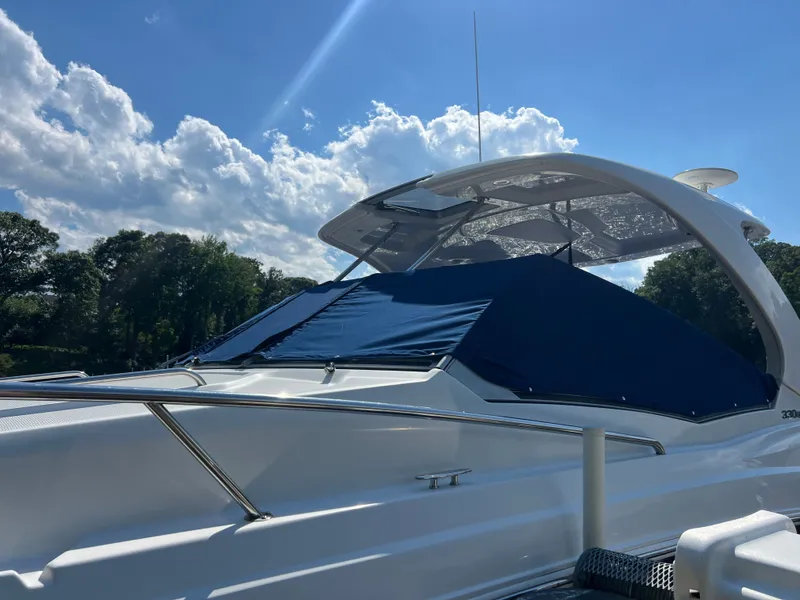 Slide: The Image of A 2013 Chaparral 330 Signature with a blue cover, set against a wooded shoreline and blue sky. - 34