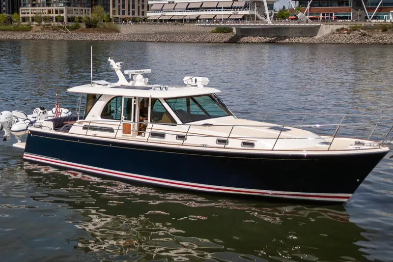 The Image of 2023 Sabre 45 Salon Express yacht cruising on a calm river near urban buildings. - 0