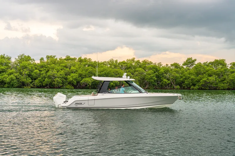 Slide: The Image of A 2027 Boston Whaler 330 Vantage cruising on calm water with a lush green shoreline. - 4