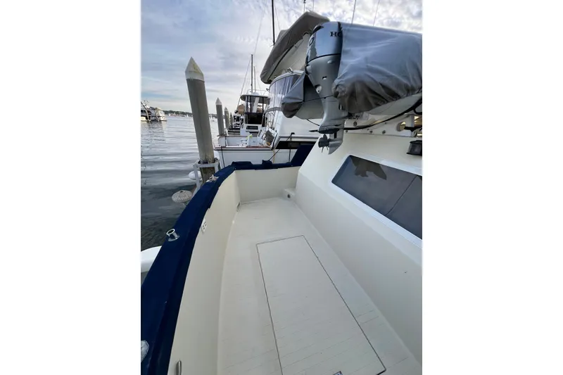 Slide: The Image of 1985 Tollycraft 48 Cockpit Motor Yacht docked, showcasing spacious deck and outboard motor. - 16