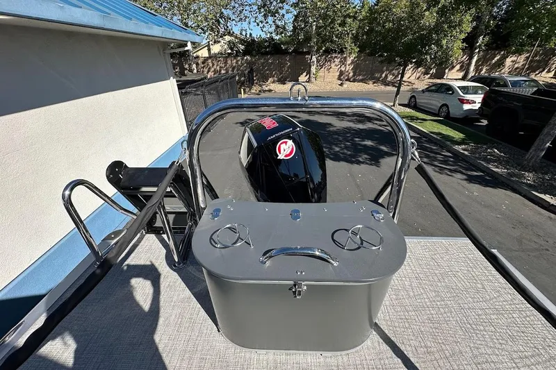 Slide: The Image of 2026 Tahoe Pontoon LTZ Quad Lounger Shift 23 with outboard motor, parked outdoors. - 29