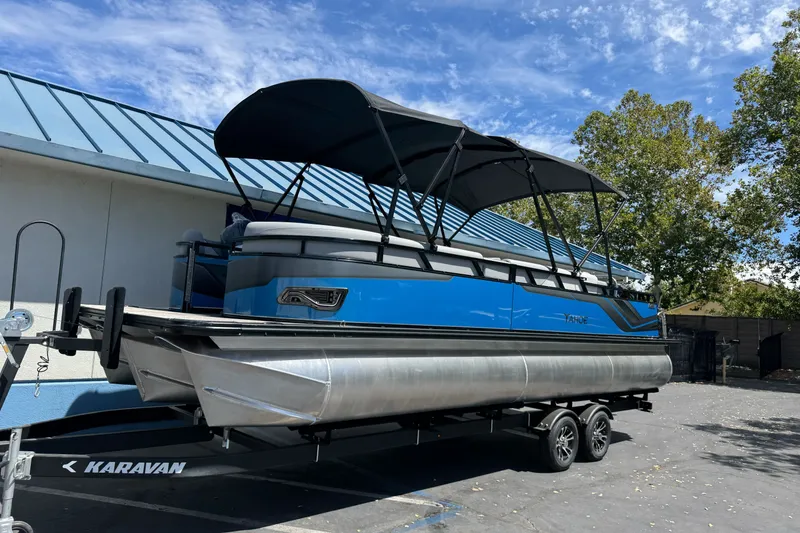 Slide: The Image of 2026 Tahoe Pontoon Sport 85 Elite Windshield 25 on trailer, blue exterior, parked outdoors. - 1