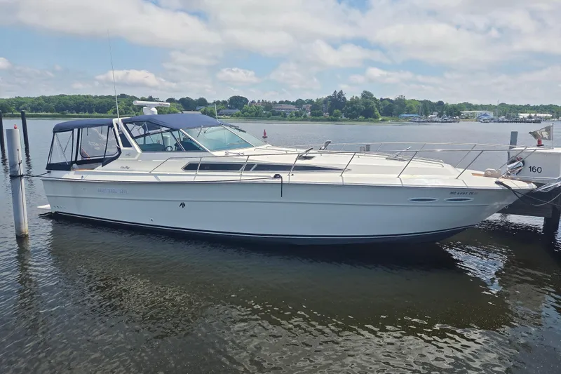 The Image of 1991 Sea Ray 390 Express Cruiser docked on a calm lake under a partly cloudy sky. - 0