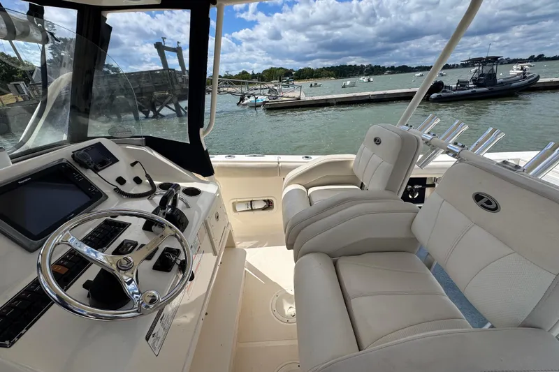 Slide: The Image of 2011 Pursuit C 280 Center Console boat interior with steering wheel and seating, docked by the water. - 5
