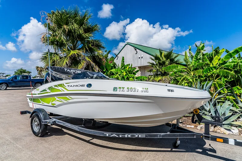 The Image of A white 2021 Tracker Tahoe boat on a trailer, surrounded by palm trees and a blue sky. - 1