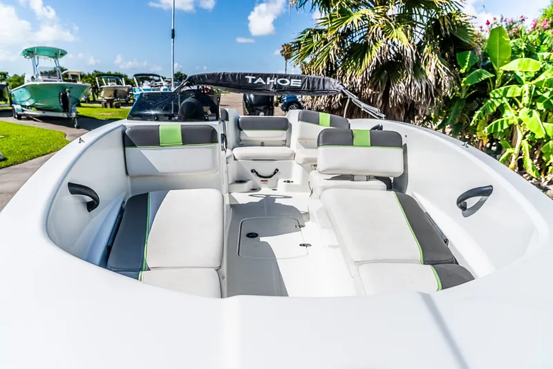 Slide: The Image of A 2021 Tracker Tahoe boat with white and gray seating, surrounded by tropical plants. - 7