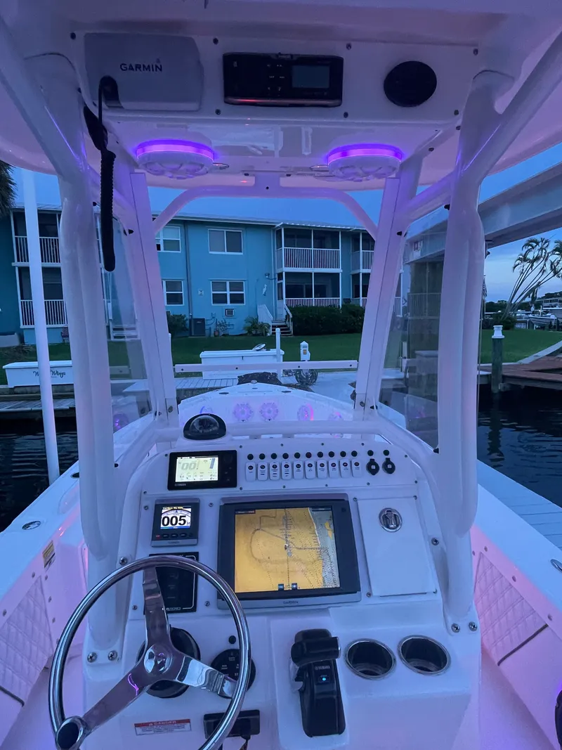 Slide: The Image of The image shows the cockpit of a 2012 Everglades 243 Center Console boat. It features a modern helm with a large display and various controls. Purple lighting creates an ambient atmosphere. Buildings and a waterway are visible in the background. - 13