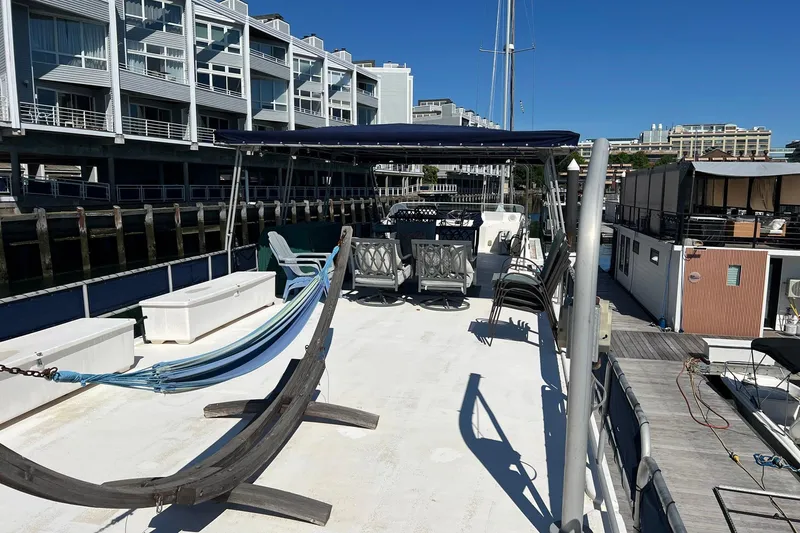 Slide: The Image of 1993 Sumerset houseboat with spacious deck, hammock, and seating, docked near modern buildings. - 30