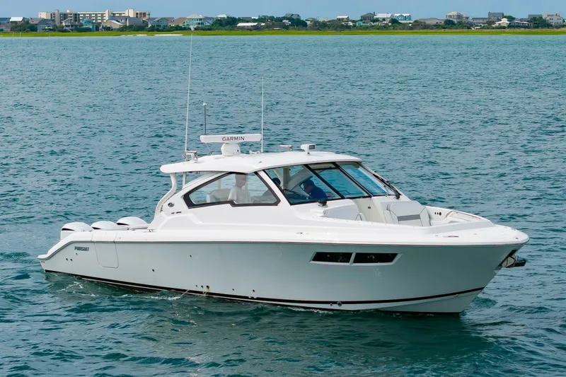 Slide: The Image of A 2021 Pursuit DC 365 Dual Console boat on calm water with coastal buildings in the background. - 8