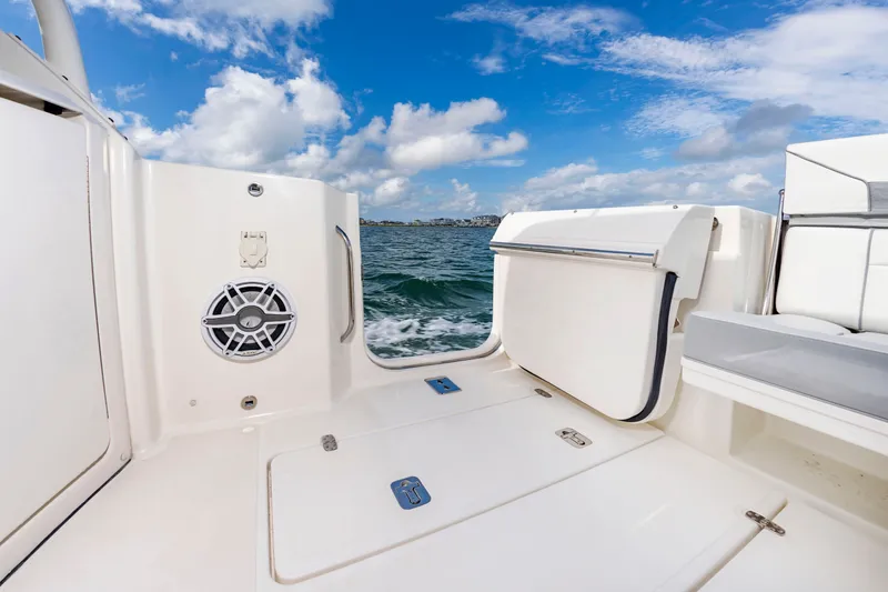 Slide: The Image of The image shows the deck of a 2021 Pursuit DC 365 Dual Console boat. It features a white surface with a built-in speaker and a fold-down compartment. The sea is visible in the background under a blue sky. - 21