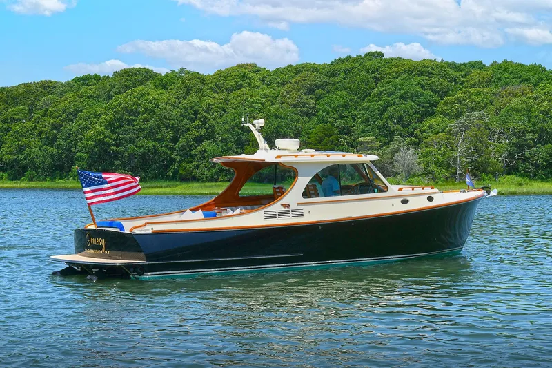Slide: The Image of 2015 Hinckley Talaria 34 yacht cruising on a serene lake with lush green forest backdrop. - 4