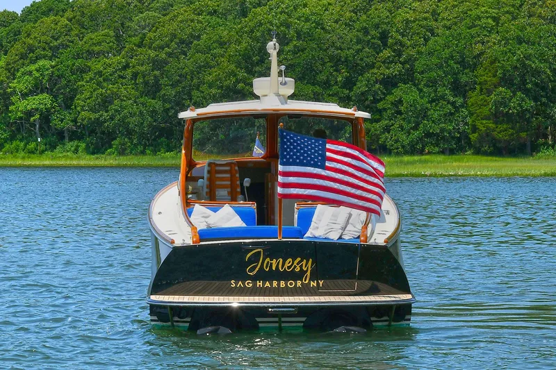 Slide: The Image of Hinckley Talaria 34 boat, 2015 model, on water with American flag, lush green background. - 1