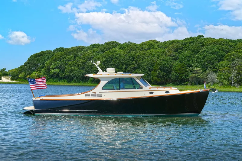 Slide: The Image of 2015 Hinckley Talaria 34 yacht cruising on a serene lake with lush green forest backdrop. - 3