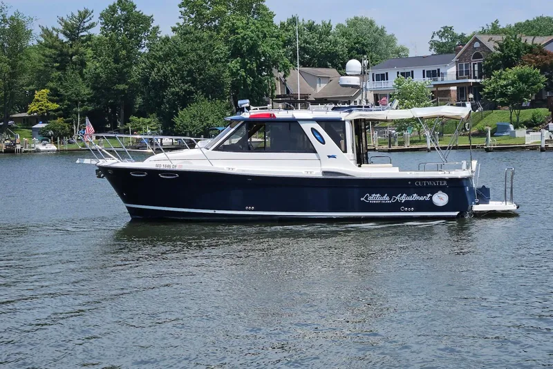 The Image of 2013 Cutwater 28 boat on a serene lake with lush greenery and houses in the background. - 0