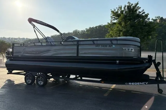 Slide: The Image of 2024 Regency 250 DL3 pontoon boat on trailer, parked outdoors in sunlight. - 11