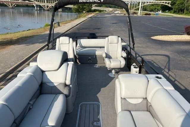 Slide: The Image of 2024 Regency 250 DL3 pontoon boat with spacious seating, docked by a scenic riverside. - 13