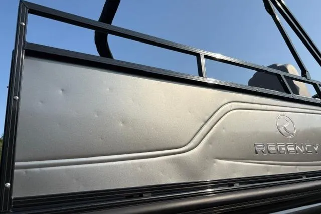 Slide: The Image of 2024 Regency 250 DL3 pontoon boat side panel with logo, under clear blue sky. - 14