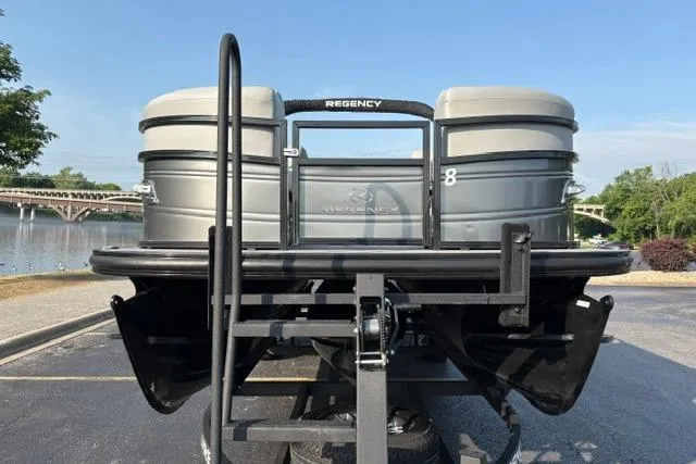 Slide: The Image of 2024 Regency 250 DL3 pontoon boat on trailer, parked near a scenic waterfront. - 2