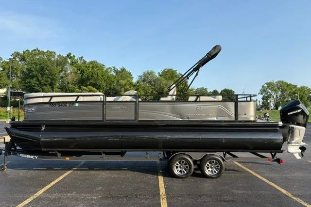 Slide: The Image of 2024 Regency 250 DL3 pontoon boat on trailer, parked in a lot with trees in background. - 4