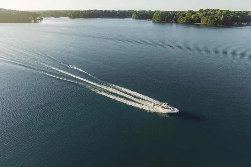 Slide: The Image of A 2027 Sea Ray SDX 270 Outboard speeds across a calm lake, surrounded by trees. - 5