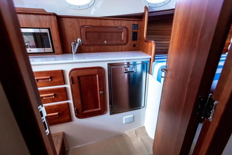 Slide: The Image of Interior of 2022 Hinckley 35 yacht featuring a compact kitchen with wood cabinetry. - 22