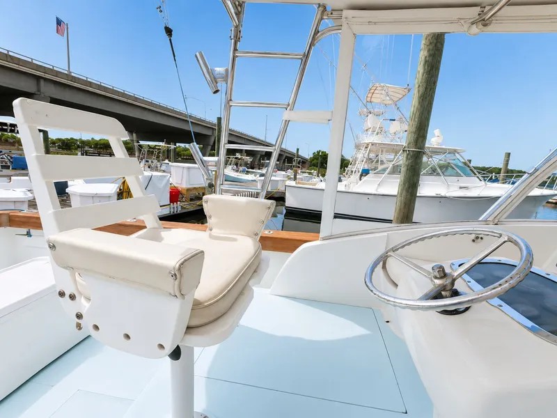 Slide: The Image of A helm station with a white seat and steering wheel, boats and a bridge in the background. - 23