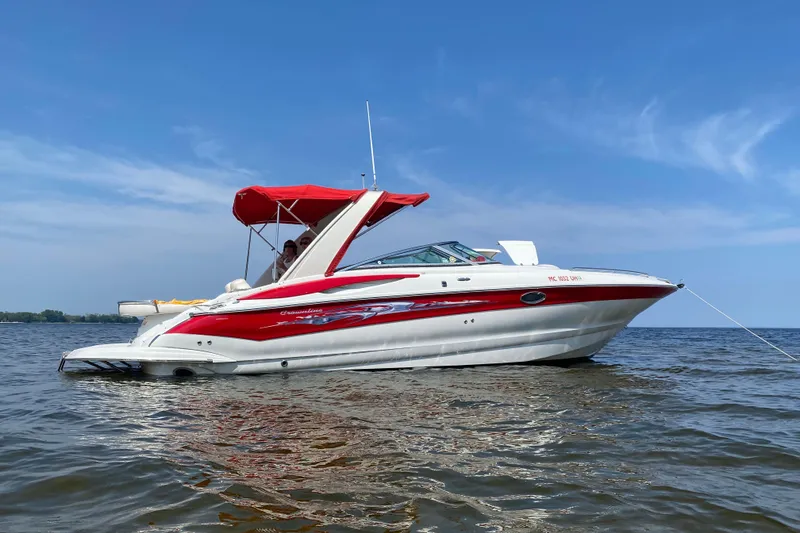 The Image of 2008 Crownline 320 LS boat with red accents anchored on a calm lake. - 0