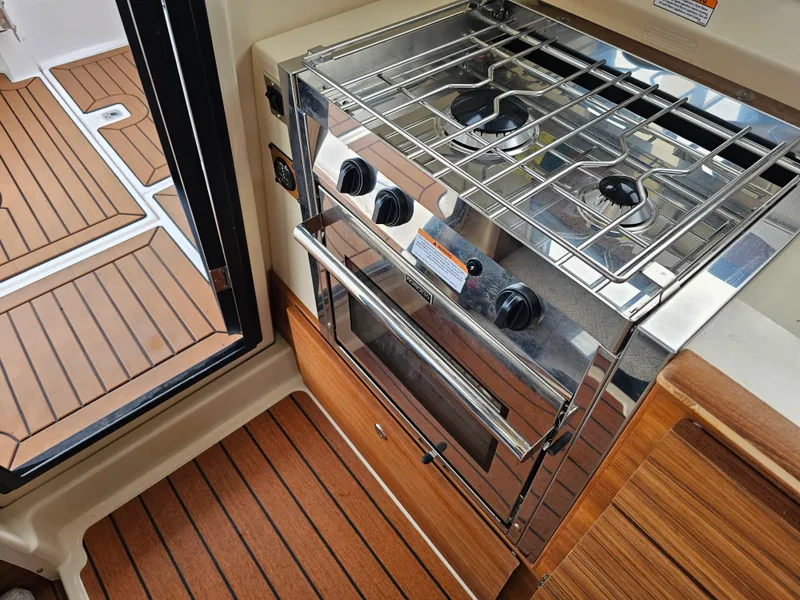 Slide: The Image of The galley of a 2025 Ranger Tugs R-27 with a stainless steel stove and wood paneling. - 29