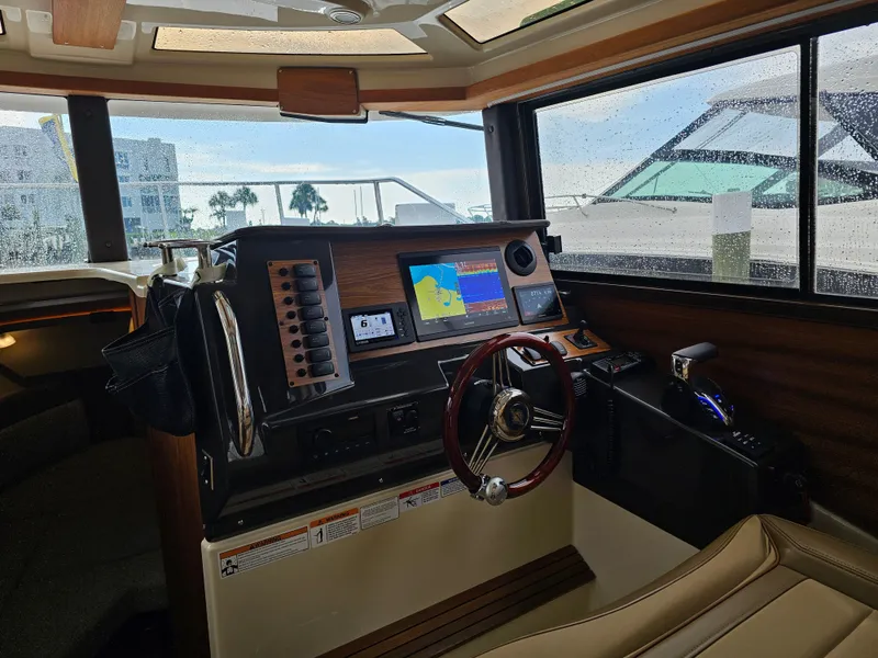 Slide: The Image of The cockpit of a 2025 Ranger Tugs R-27 with modern navigation electronics and a wooden steering wheel. - 13