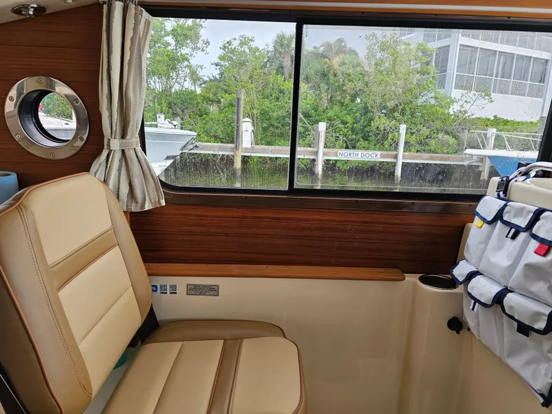 Slide: The Image of Interior of a 2025 Ranger Tugs R-27 with beige seating and a window view of a dock. - 18