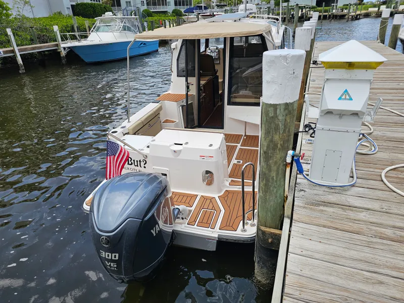 Slide: The Image of A 2025 Ranger Tugs R-27 docked at a wooden pier. The outboard motor is visible. - 12