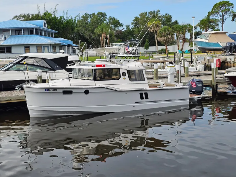 Slide: The Image of A white 2025 Ranger Tugs R-27 boat docked at a marina, surrounded by other boats. - 1
