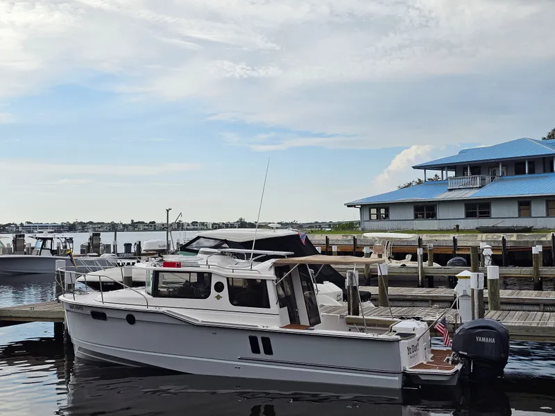 Slide: The Image of A 2025 Ranger Tugs R-27 is docked. A building with a blue roof is visible in the background. - 2