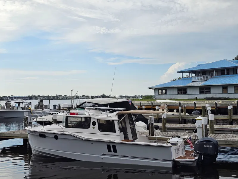 Slide: The Image of A 2025 Ranger Tugs R-27 is docked at a calm pier with a building in the background. - 2