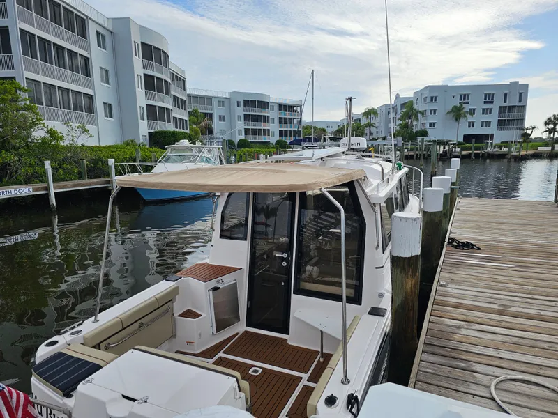 Slide: The Image of A 2025 Ranger Tugs R-27 docked at a modern marina with surrounding buildings. - 5