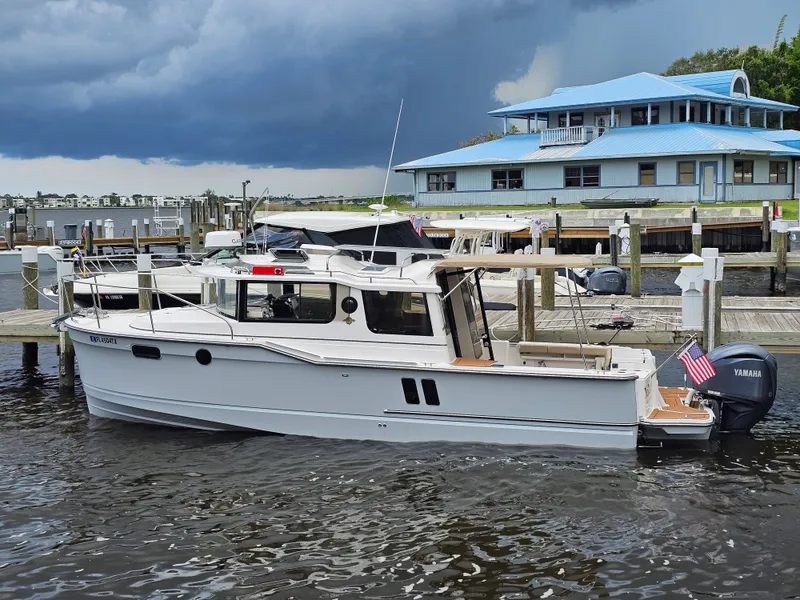 Slide: The Image of A 2025 Ranger Tugs R-27 is docked. A building with a blue roof is visible in the background. - 6
