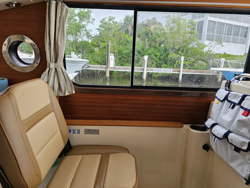 Slide: The Image of Interior of a 2025 Ranger Tugs R-27 with beige seating and a window view of a dock. - 18