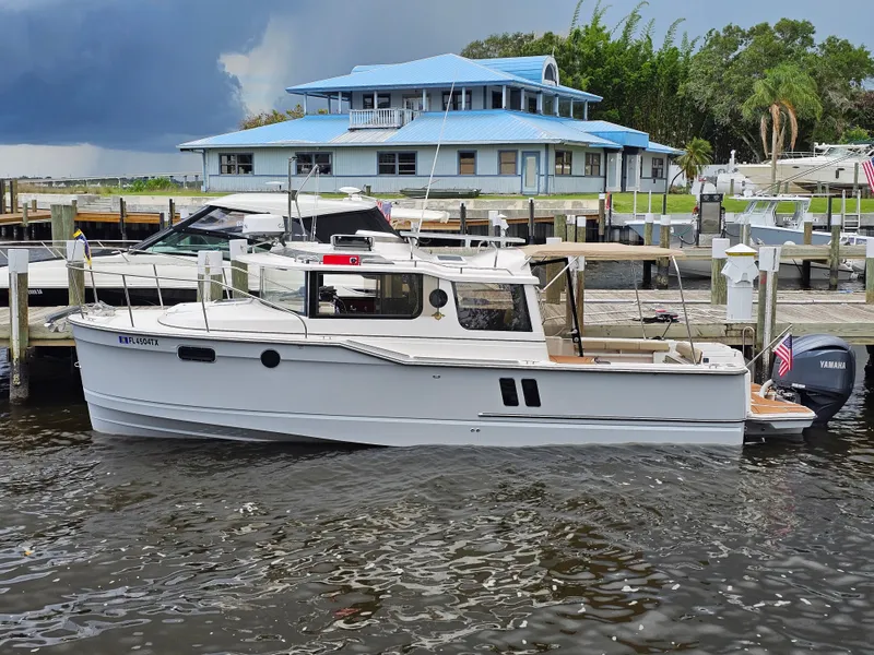 Slide: The Image of A 2025 Ranger Tugs R-27 docked near a blue building, with a Yamaha outboard motor. - 7