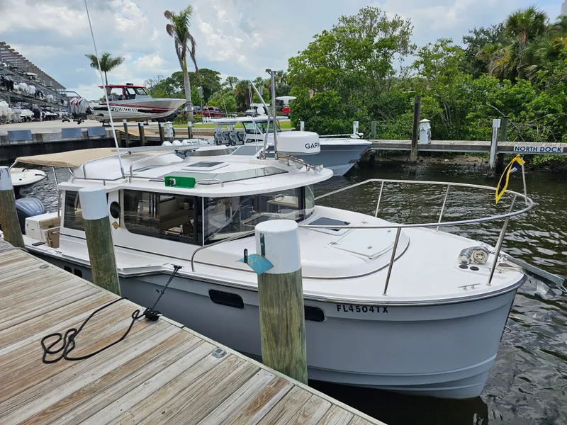 Slide: The Image of A white 2025 Ranger Tugs R-27 boat docked at a wooden pier in a calm harbor. - 11