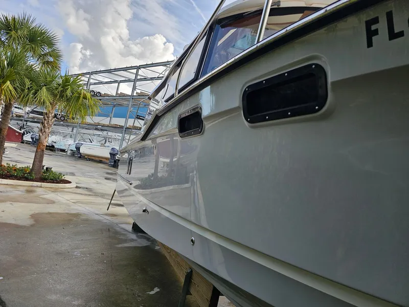 Slide: The Image of A 2025 Ranger Tugs R-27 is on a dry dock. Palm trees and other boats are visible in the background. - 38