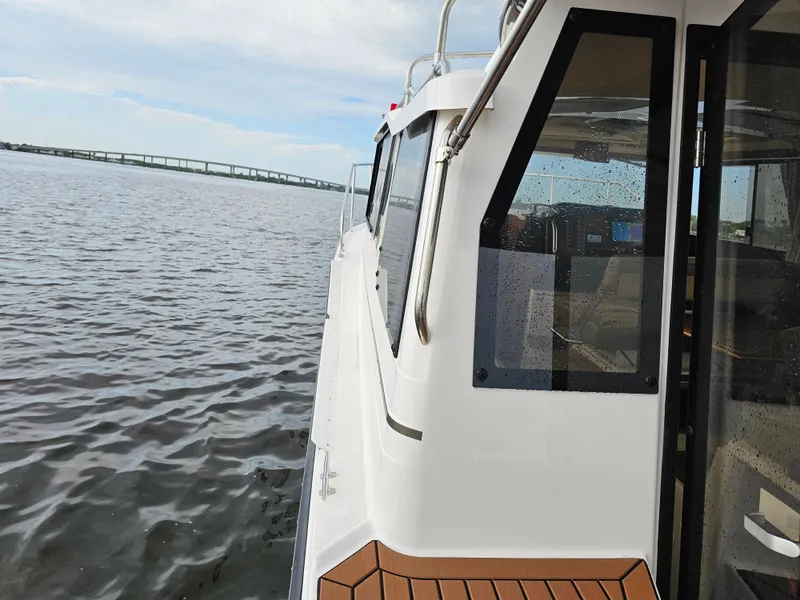 Slide: The Image of A modern boat with white walls and wood decks cruises on calm water under a blue sky. - 35