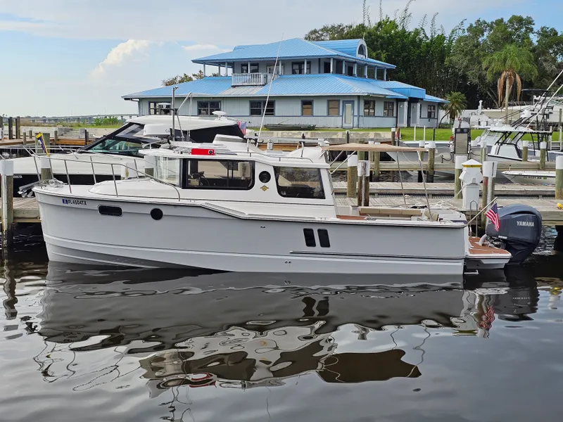 The Image of A white 2025 Ranger Tugs R-27 boat docked in front of a building with a blue roof. - 0